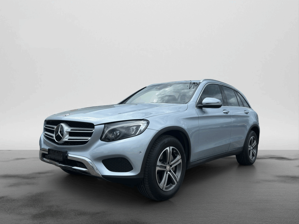 Silberner Mercedes-Benz SUV steht auf nassem Asphalt vor neutralem, grauem Hintergrund. Das Fahrzeug ist leicht von vorne links aufgenommen und wirkt gepflegt und modern.