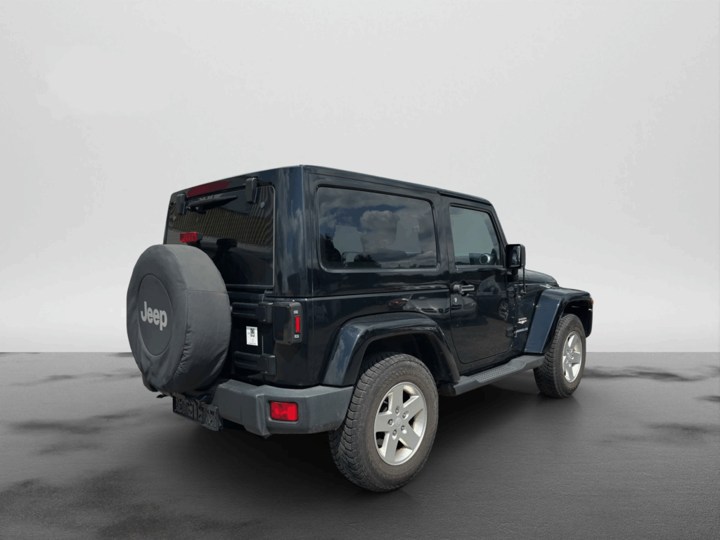 ChatGPT: Schwarzer Jeep Geländewagen, schräg von hinten rechts aufgenommen. Am Heck ist ein Ersatzrad mit Jeep-Abdeckung befestigt. Das Fahrzeug steht auf nassem Asphalt vor neutralem, grauem Hintergrund.